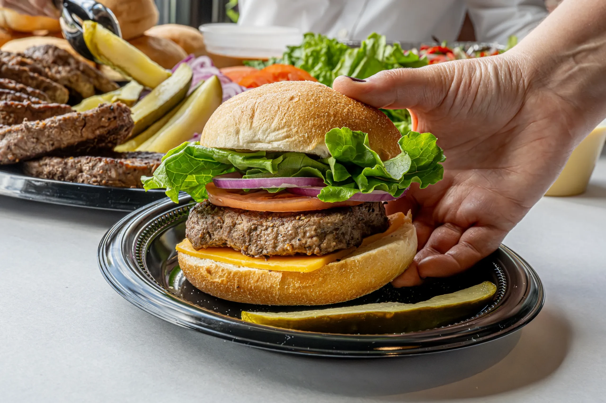 DSC_7487-Enhanced-NR A cheeseburger being picked up with patties and pickles in the background